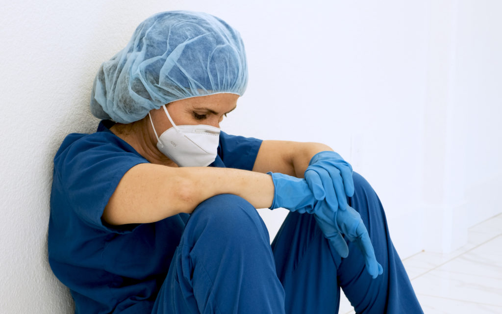 Caucasian Overworked, sad, tired, female healthcare worker sitting on the floor of a hospital corridor