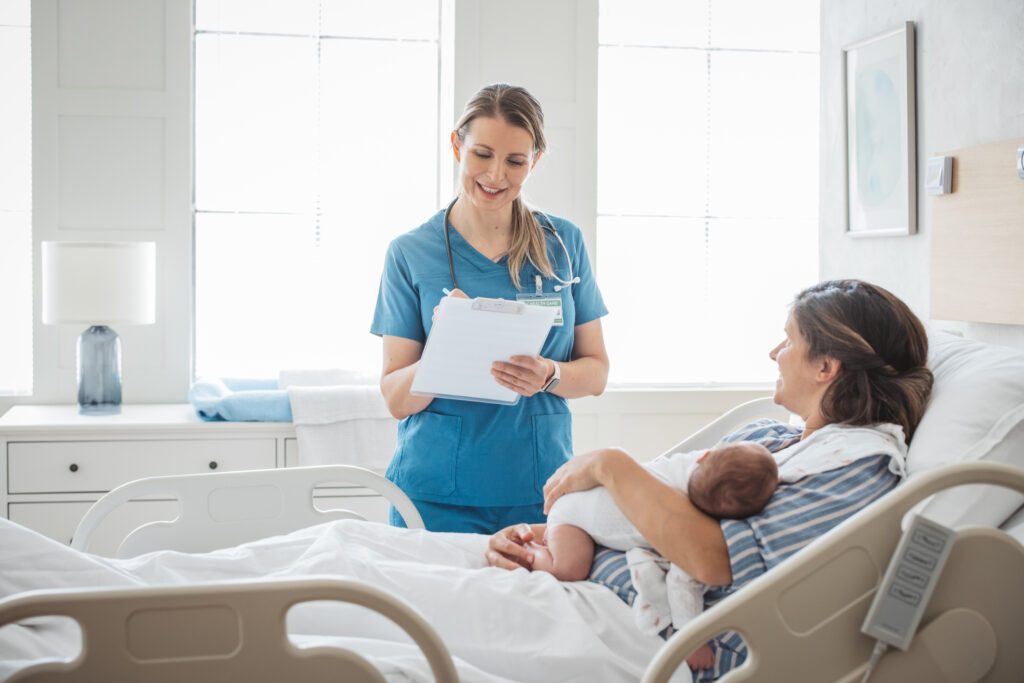 Nurse taking personal data from mother and talking to her. Mother holding newborn baby.